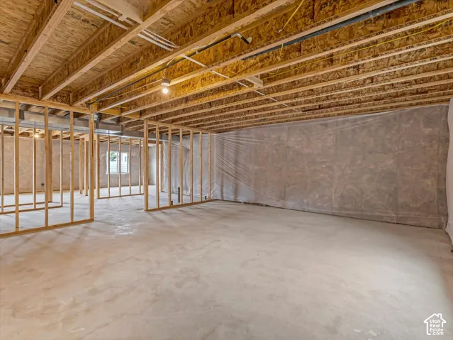 Unfinished basement with concrete flooring, framed wall sections, exposed ceiling joists, and a visible window