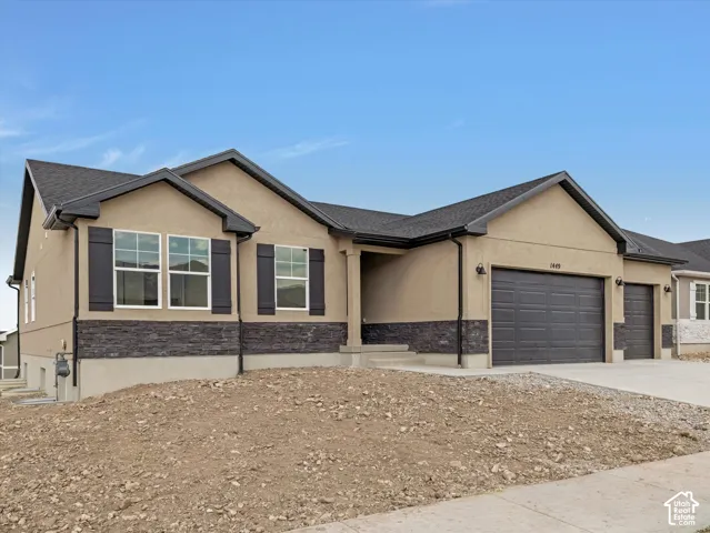 Stucco exterior with dark stone accents, multiple windows with dark shutters, attached two-car garage, and concrete driveway