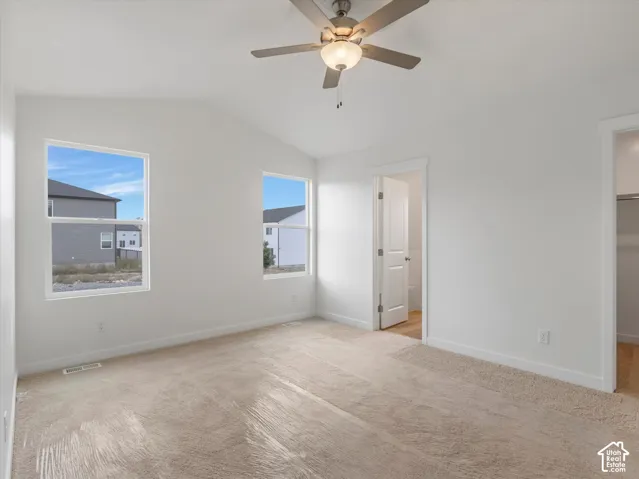 Vaulted ceiling with a ceiling fan, two windows, wall-to-wall carpeting, and a white interior door