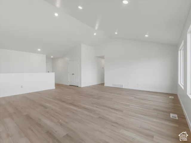 Vaulted ceilings with recessed lighting, light wood-finish flooring, and white walls create an airy ambiance