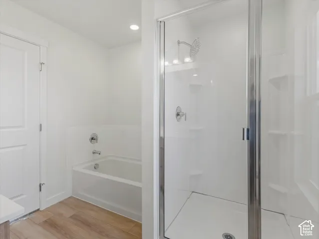 Walk-in shower with a glass enclosure, separate soaking tub, and wood-finish flooring