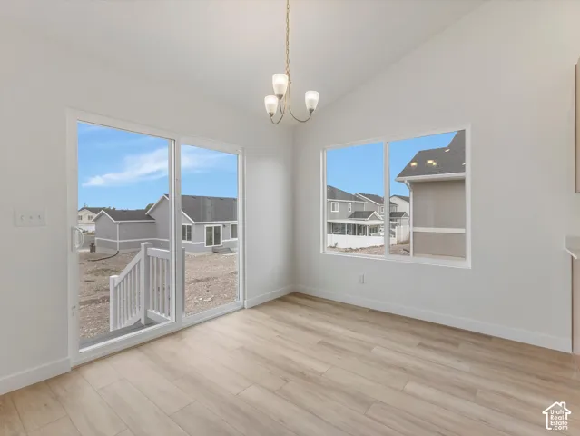 Vaulted ceiling with an attached chandelier, wood-finish flooring, sliding glass door, and a multi-pane window