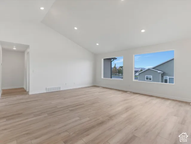 Vaulted ceiling with recessed lighting, large windows, and wood-finish flooring