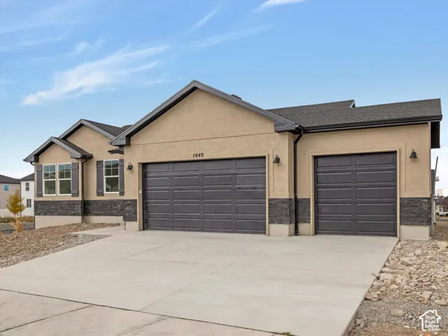 Stucco exterior with stacked stone accents, multiple garage doors, and dark-framed windows with shutters