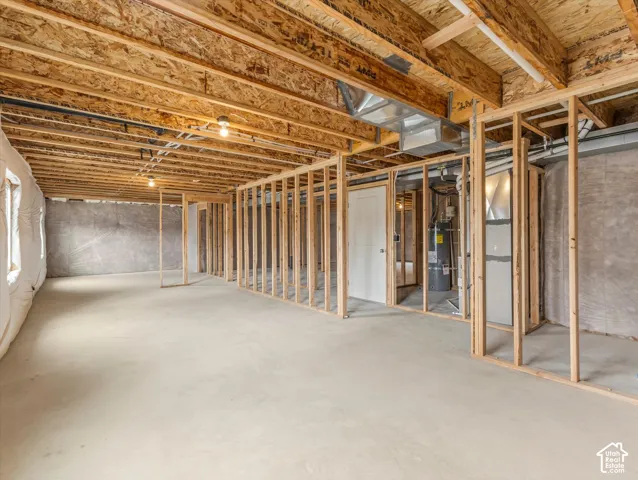 Unfinished lower level with wood framing, concrete flooring, exposed ceiling joists, and a partial wall with a white door