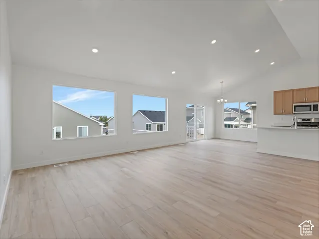 Open-concept living space featuring vaulted ceilings, recessed lighting, expansive windows, wood-finish flooring, and a kitchen with wood cabinetry