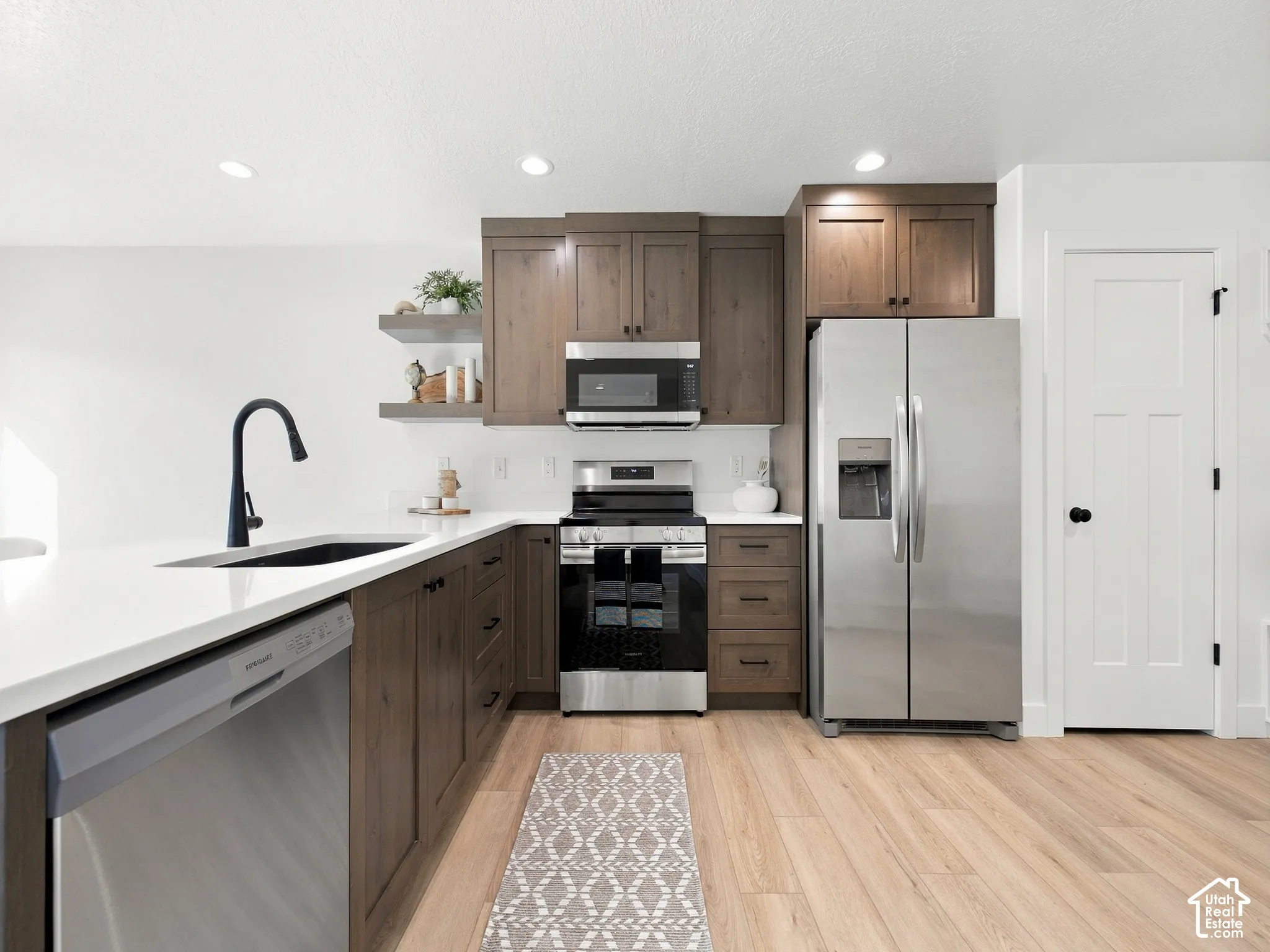 Kitchen featuring wood-finish flooring, stainless steel appliances, white countertops, dark wood-finish cabinetry, and recessed lighting