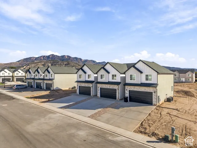 Modern townhome architecture featuring light gray siding with dark trim, stone veneer accents, and attached two-car garages