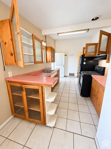 Kitchen featuring tile flooring, wood cabinetry with some glass-front doors, a double basin sink, and laminate countertops