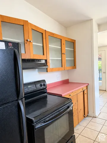 Kitchen featuring black appliances, wood-finish cabinetry with frosted glass inserts, red countertops, and tiled flooring
