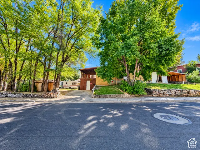 Mature trees providing shade, stone retaining walls, sloped lawn, and a paved driveway