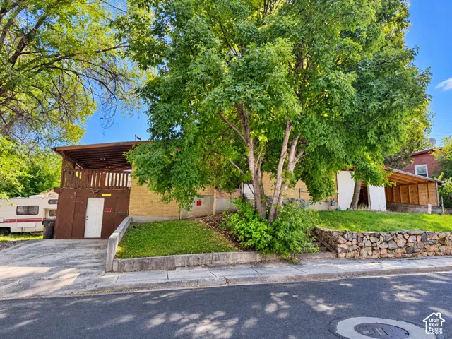 Paved driveway leading to a brown wood-paneled structure with an upper deck, complemented by a stone retaining wall and mature trees