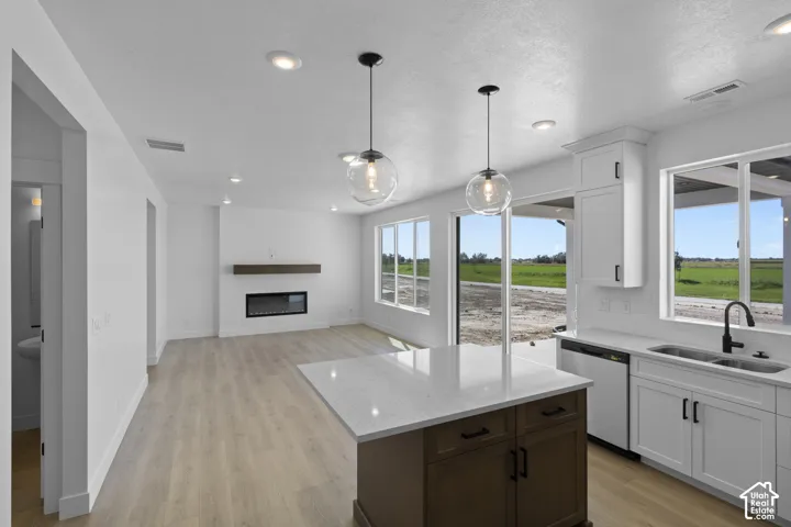 Wood-finish flooring throughout, kitchen island with a light-toned countertop, white cabinetry with matte black hardware, recessed lighting, and a linear electric fireplace