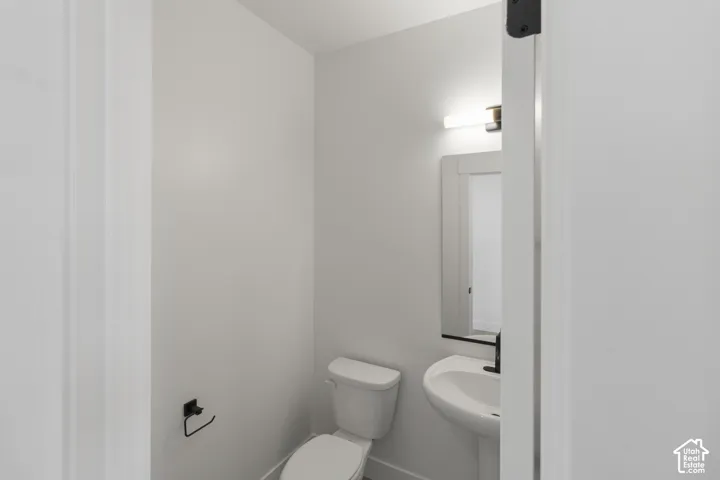 Pedestal sink with a matte black faucet, wall-mounted mirror, and contemporary light fixture