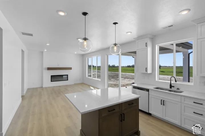 Open-concept living area featuring wood-finish flooring, a contemporary fireplace with a wood mantle, recessed lighting, and a kitchen island with a light-colored countertop