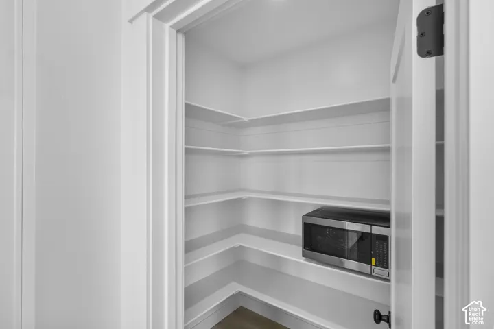 Spacious pantry featuring multiple built-in shelves, white walls, and wood-finish flooring