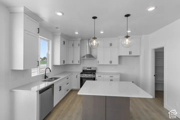 Kitchen featuring white shaker cabinetry, stainless steel appliances, light-toned wood-finish flooring, a kitchen island with stone countertops, and recessed lighting