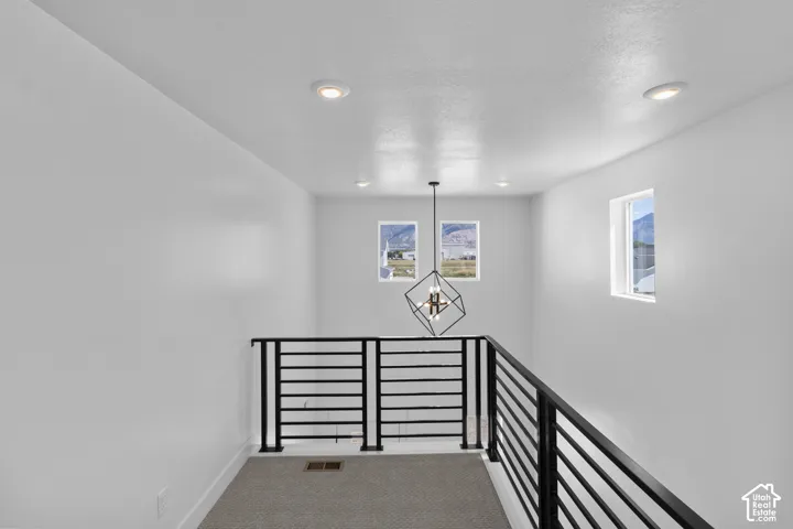 Modern black metal railing, contemporary geometric chandelier, recessed ceiling lighting, and windows providing natural illumination