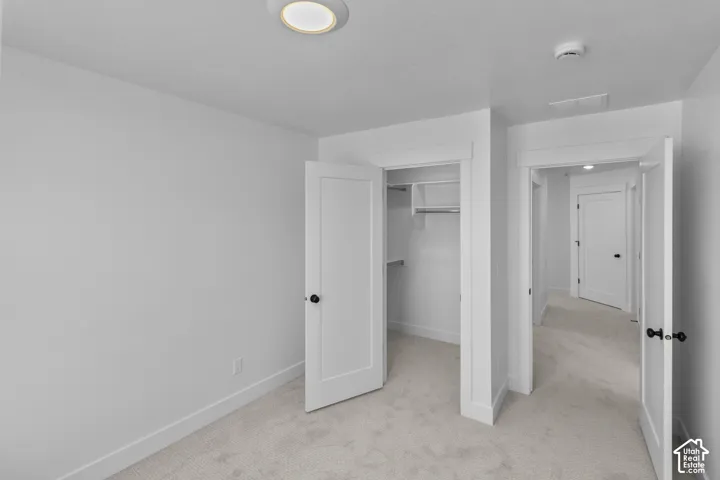 Light-colored carpeting, white walls, white trim, recessed ceiling light, and a built-in closet with shelving and hanging rod