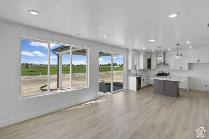 Open-concept living space with wood-finish flooring, white cabinetry, a kitchen island, stainless steel appliances, and a sliding glass door