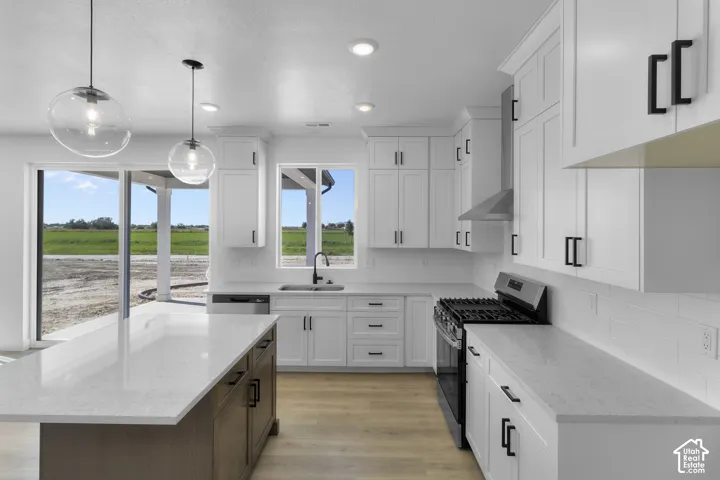 Kitchen featuring white shaker-style cabinetry, light-toned countertops, a center island with contrasting base, stainless steel appliances, and light wood-finish flooring
