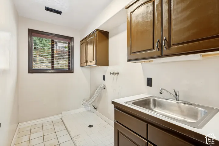 Utility room featuring a window, overhead cabinetry, a built-in sink with countertop, and tile flooring