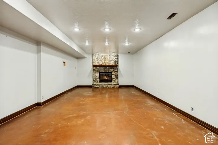Stone-clad fireplace with a wood mantle, recessed lighting, and concrete flooring