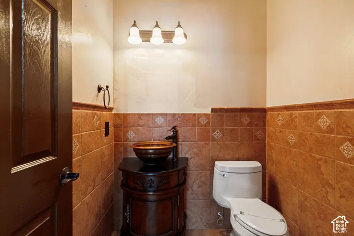 Powder room featuring a freestanding vanity with vessel sink, wall-mounted light fixture, and tile wainscoting with decorative accents