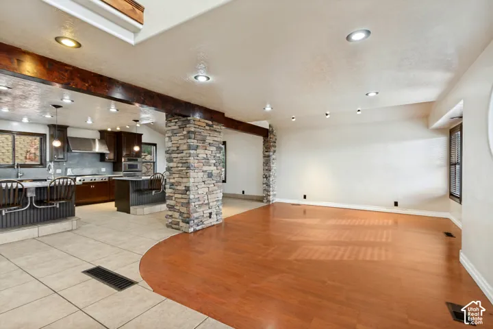 Open-concept living area with wood-finish flooring, stone-clad architectural elements, recessed lighting, and a kitchen featuring dark wood cabinetry and stainless steel appliances