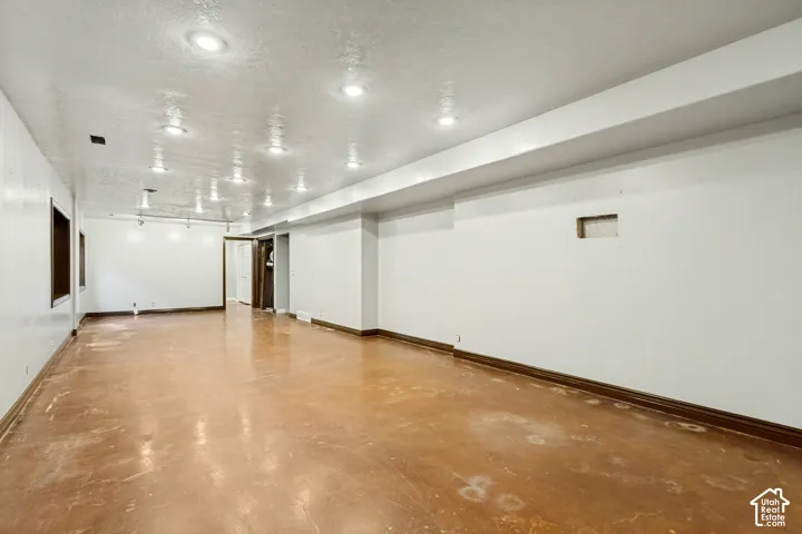 Expansive room with recessed lighting, stained concrete flooring, white walls, and wood-trim doorways