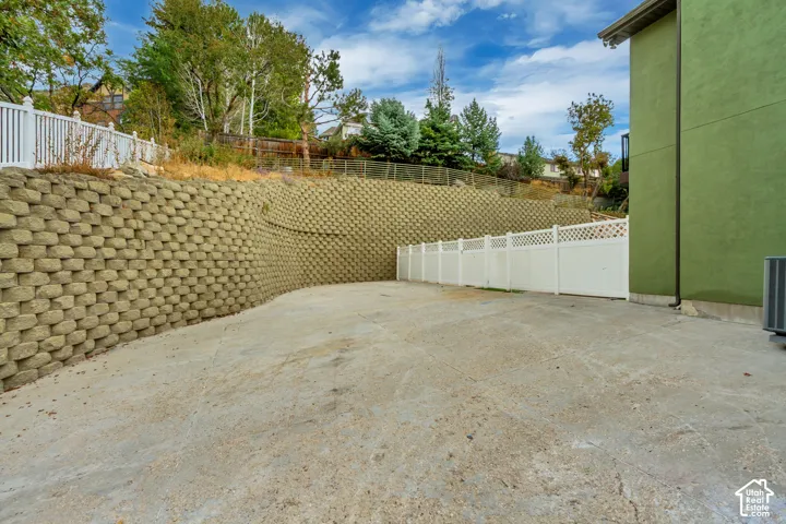 Concrete-paved ground with block retaining walls, vinyl lattice-top fencing, and a stucco exterior