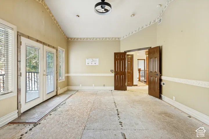 Vaulted ceiling with a flush-mount ceiling fan, double French doors, two windows with blinds, and solid wood interior doors