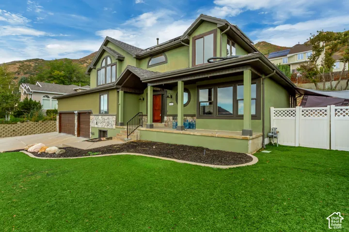 Exterior featuring a covered porch, stone accent siding, multi-pane windows, a two-car garage, and a lush green lawn