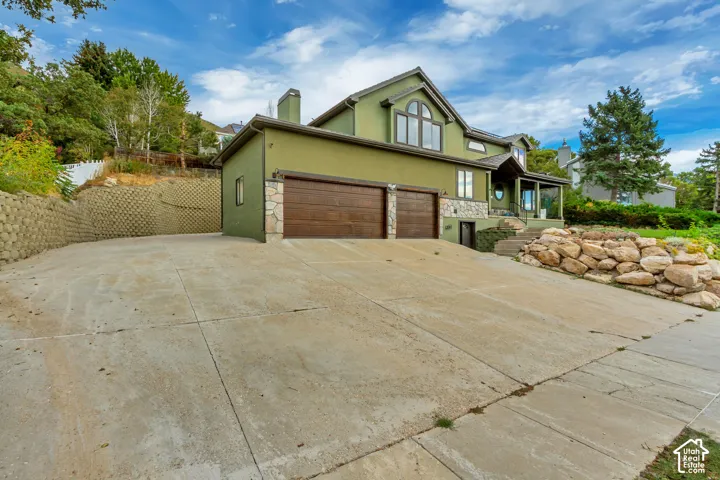 Stucco exterior with stone accents, two-car garage with wood-finish doors, covered entry porch, and a concrete driveway