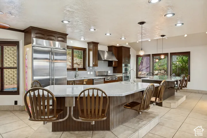 Kitchen featuring stainless steel appliances, dark wood cabinetry, a large center island with seating, pendant lighting, and recessed ceiling lights