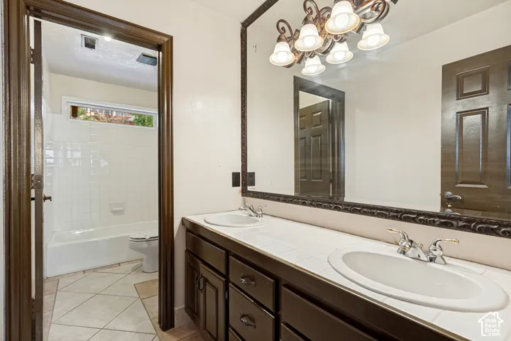 Dual vanity with integrated sinks, tiled countertop, dark wood-finish cabinetry, and an ornate framed mirror
