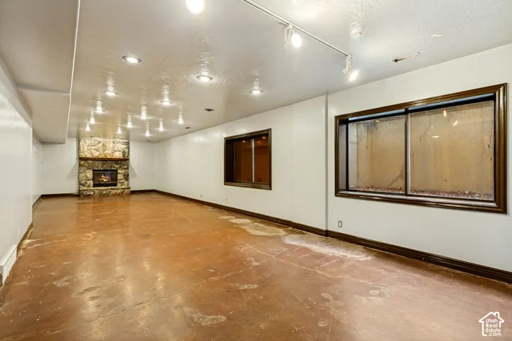 Spacious room featuring a stone-clad fireplace, recessed lighting, track lighting, and two windows with dark trim