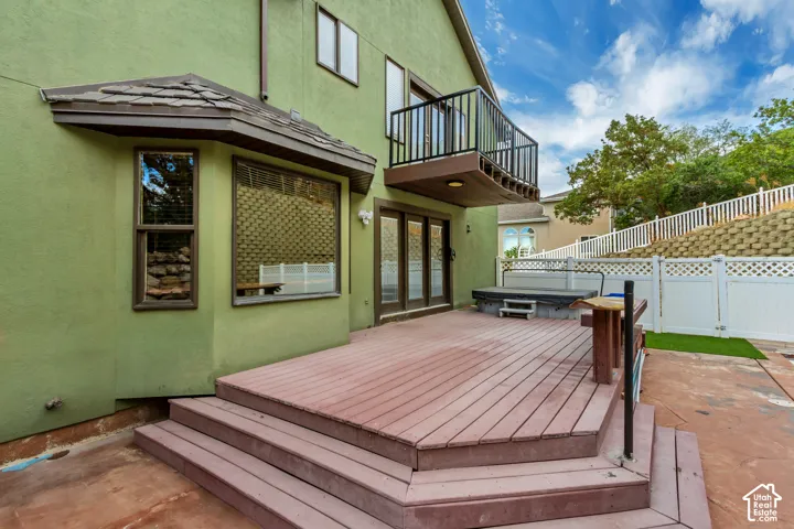 Expansive multi-level wood-finish deck with integrated steps, stucco exterior, and upper-level balcony with metal railing