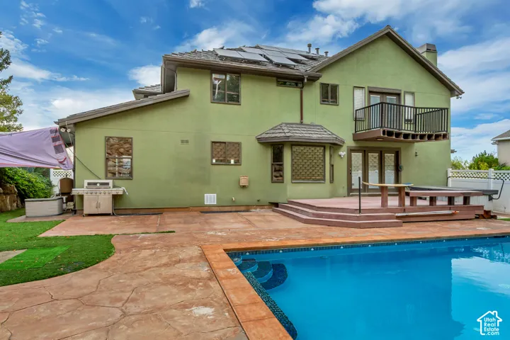 Exterior featuring a concrete patio, built-in swimming pool, multi-level deck, second-story balcony with metal railing, and rooftop solar panels