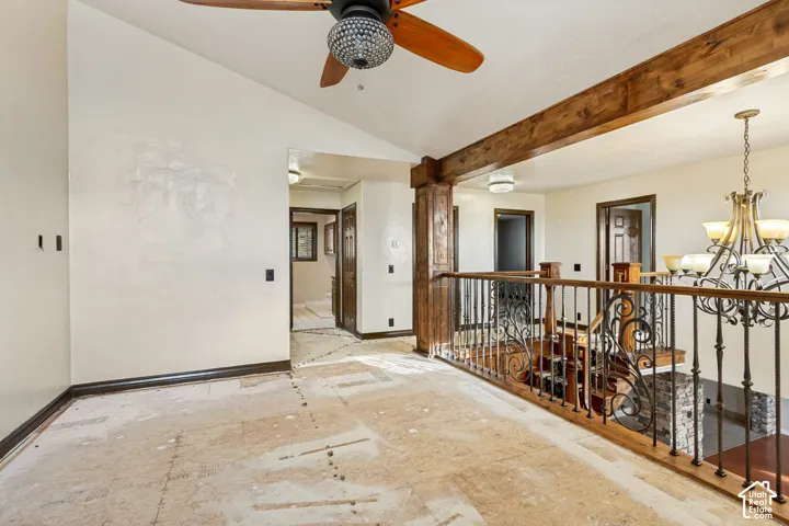 Vaulted ceiling with wood-finish beam, ornate wrought iron railing, wood-finish newel posts, and wood-finish ceiling fan