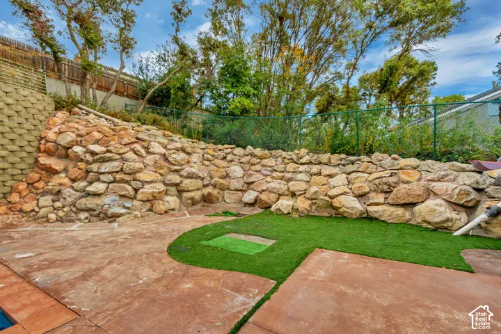 Stamped concrete patio featuring a rock retaining wall, artificial turf accents, and a block retaining wall