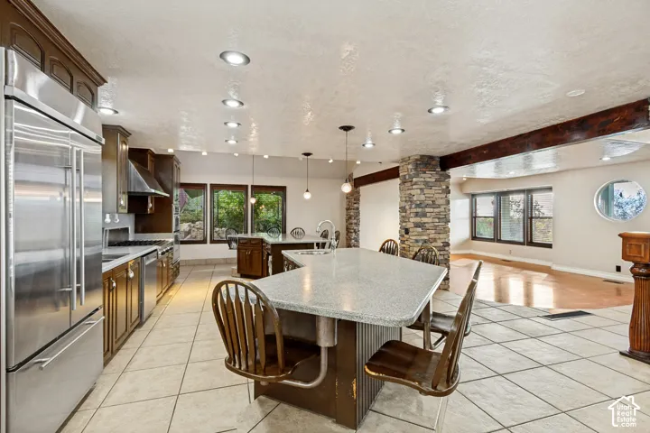 Spacious kitchen featuring stainless steel appliances, dark wood cabinetry, a large center island with a light-toned countertop, and recessed lighting