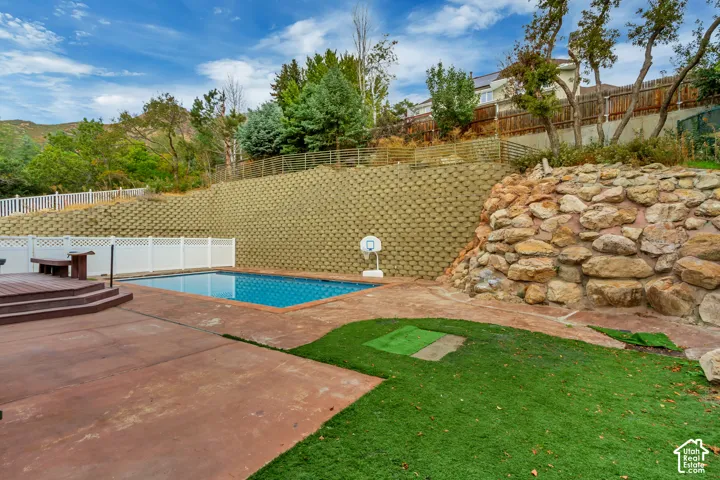 Outdoor pool with a concrete surround, wood-tone decking, and a white lattice fence