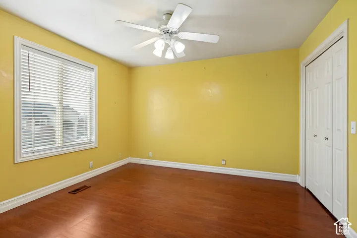 Wood-finish flooring with white baseboards, a ceiling fan with integrated lighting, a window with blinds, and white bi-fold closet doors