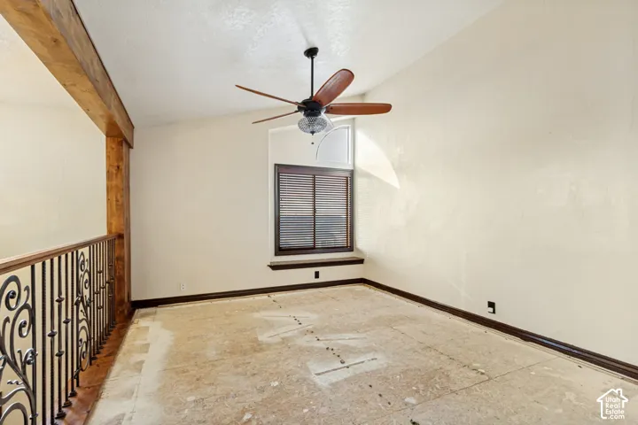 Room featuring a wood-beam accent, wrought iron railing, window with integrated blinds, and ceiling fan