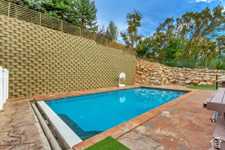 In-ground swimming pool with stamped concrete decking, retaining wall, and natural rock landscaping