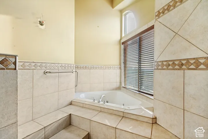 Jetted soaking tub with chrome fixtures, surrounded by neutral tile and decorative accent banding