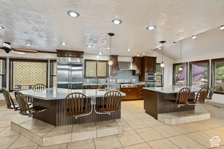 Spacious kitchen featuring two large islands with integrated seating, stainless steel appliances, extensive wood cabinetry, and a vaulted ceiling with recessed lighting