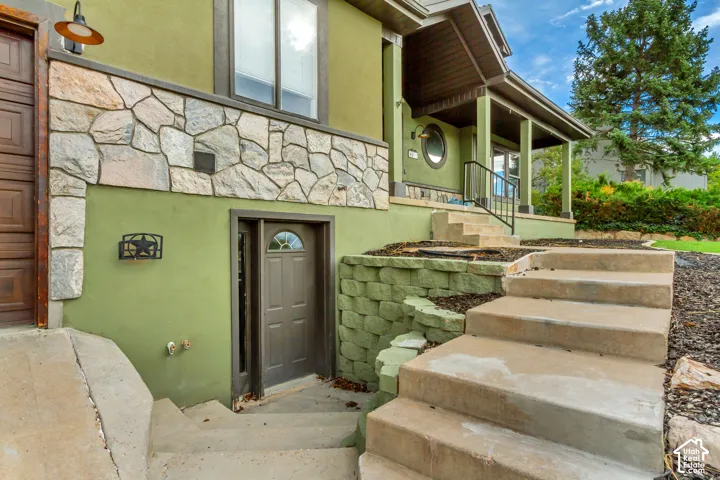 Exterior featuring a stone veneer accent, stucco siding, concrete stairs, and a covered porch