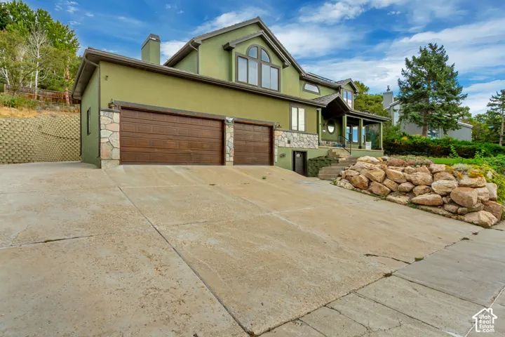 Multi-level residence featuring a stucco exterior, stone accents, two-car garage with wood-panel doors, and a covered entry porch